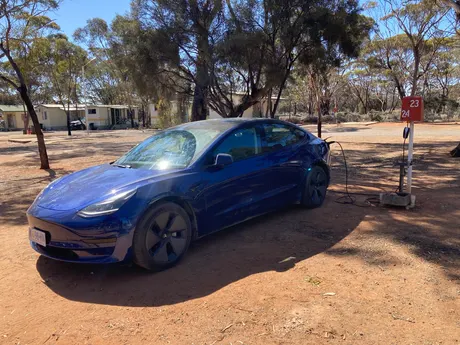 Blaues Tesla Model 3 mit Ladekabel an einer Stromsäule auf einem Campingplatz