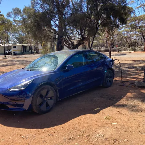 Blaues Tesla Model 3 mit Ladekabel an einer Stromsäule auf einem Campingplatz