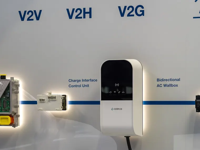 Bidirektionale AC-Wallbox auf einer Messe, darüber die Anwendungen V2V, V2H und V2G