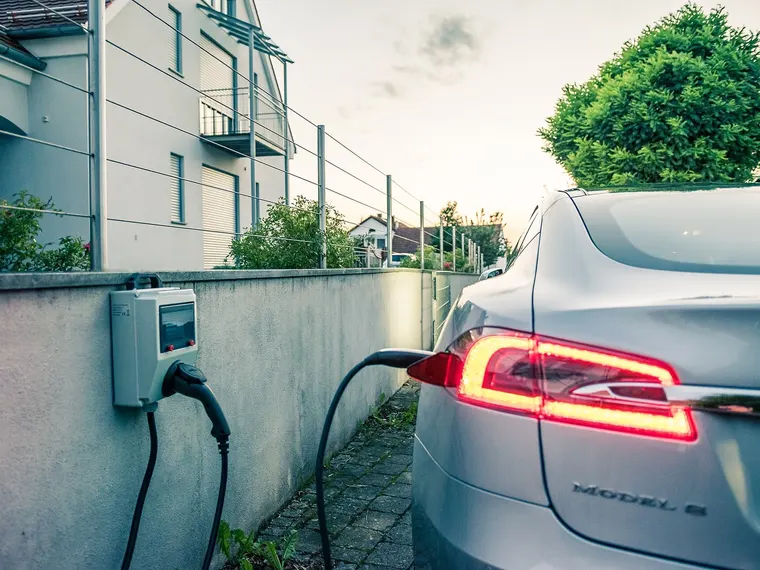 Wallbox an einer Mauer vor einem Wohnhaus, ein Elektroauto lädt