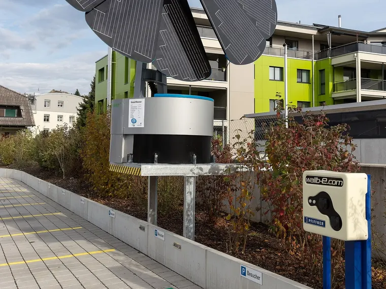 Photovoltaikanlage in Blütenform neben einer Wallbox an einer Wohnanlage