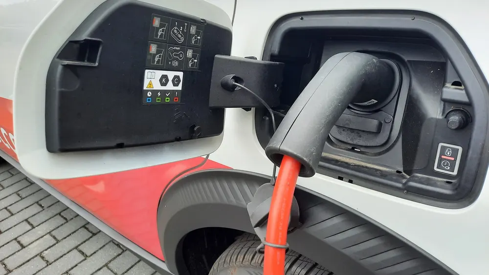 Typ-2-Ladestecker mit rotem Kabel in der Ladebuchse eines weißen E-Autos, daneben eine Taste mit Schloss-Symbol