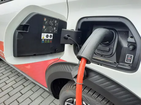 Typ-2-Ladestecker mit rotem Kabel in der Ladebuchse eines weißen E-Autos, daneben eine Taste mit Schloss-Symbol