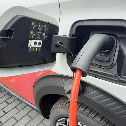 Typ-2-Ladestecker mit rotem Kabel in der Ladebuchse eines weißen E-Autos, daneben eine Taste mit Schloss-Symbol