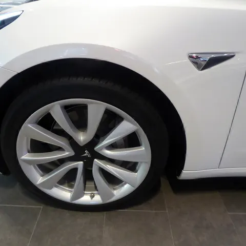 Vorderrad eines weißen Tesla Model 3 mit Leichtmetallfelge, unten am Felgenrand das Reifenventil