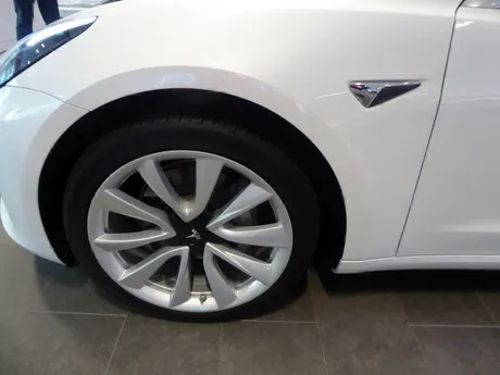 Vorderrad eines weißen Tesla Model 3 mit Leichtmetallfelge, unten am Felgenrand das Reifenventil