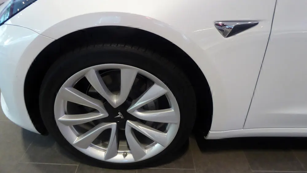 Vorderrad eines weißen Tesla Model 3 mit Leichtmetallfelge, unten am Felgenrand das Reifenventil