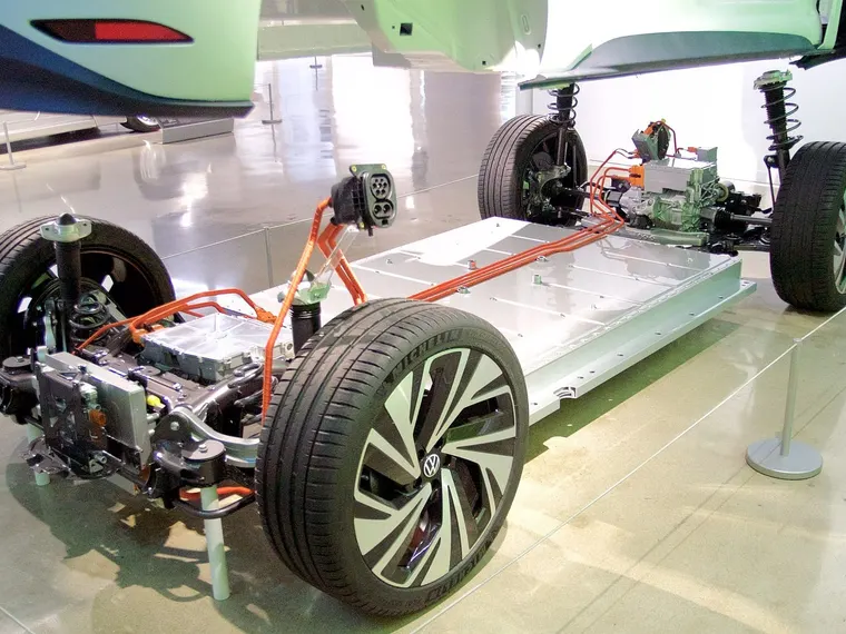 Ausgestelltes Fahrgestell eines Elektroautos (VW ID.3): Akku im Unterboden, orangefarbene Hochvoltleitungen, Ladebuchse und Elektroantrieb an der Hinterachse