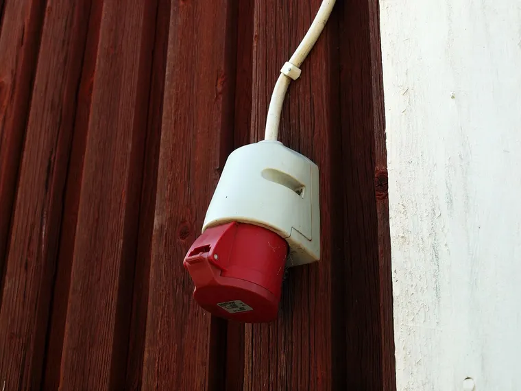 Rote CEE-Drehstromsteckdose mit geschlossenem Deckel an einer Holzwand