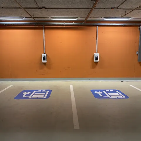 Zwei Wallboxen an der Wand einer Tiefgarage über zwei markierten Ladestellplätzen