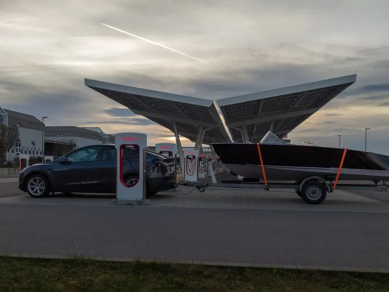 Elektroauto (Tesla Model Y) mit angekuppeltem Bootsanhänger beim Laden an einer Schnellladestation