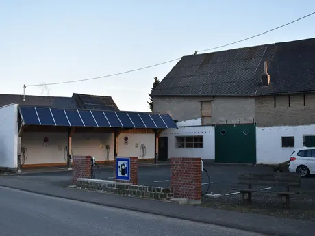 Carport mit Solarmodulen auf dem Dach und mehreren Wallboxen an einer Ladestation in Mörsdorf (Hunsrück), dahinter ein Hausdach mit PV-Anlage